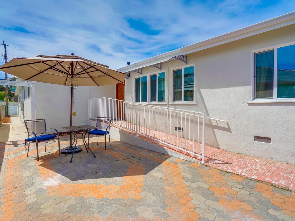 A sunny backyard patio with an umbrella, table, and chairs.