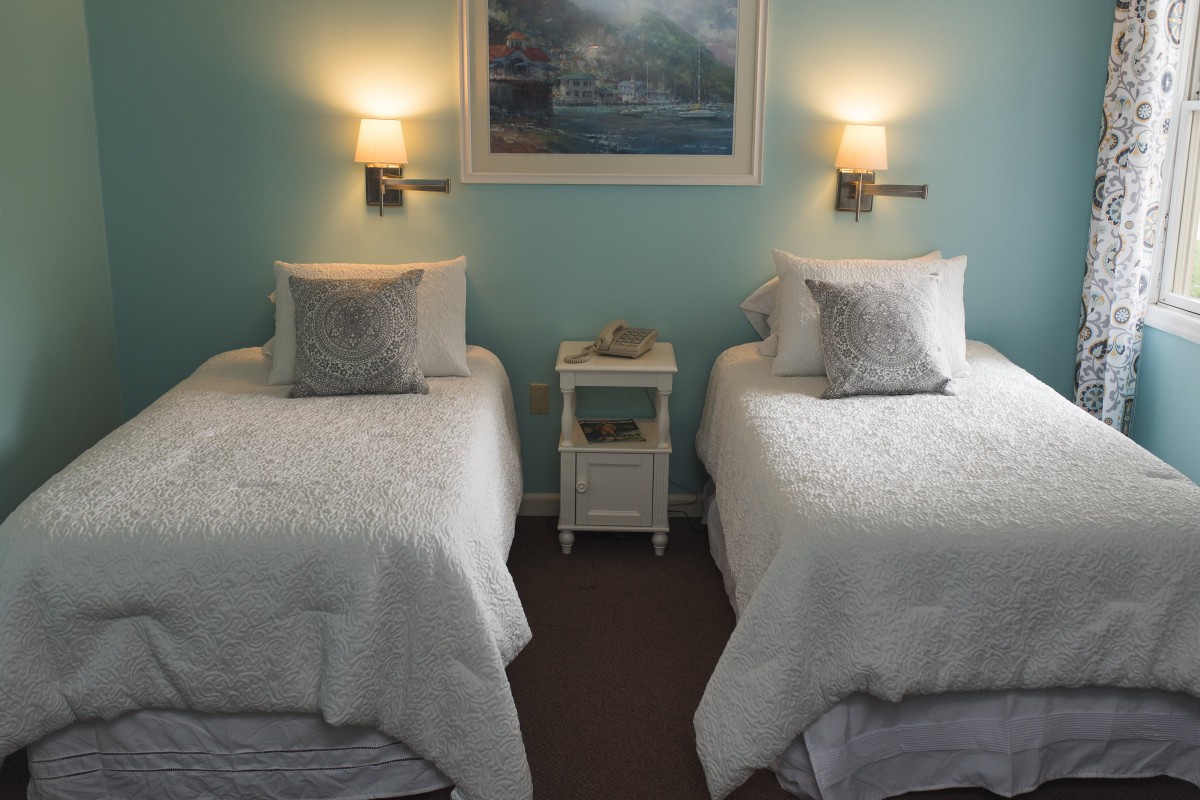 A cozy bedroom featuring two twin beds with light bedding, a shared nightstand, and soft wall lighting.