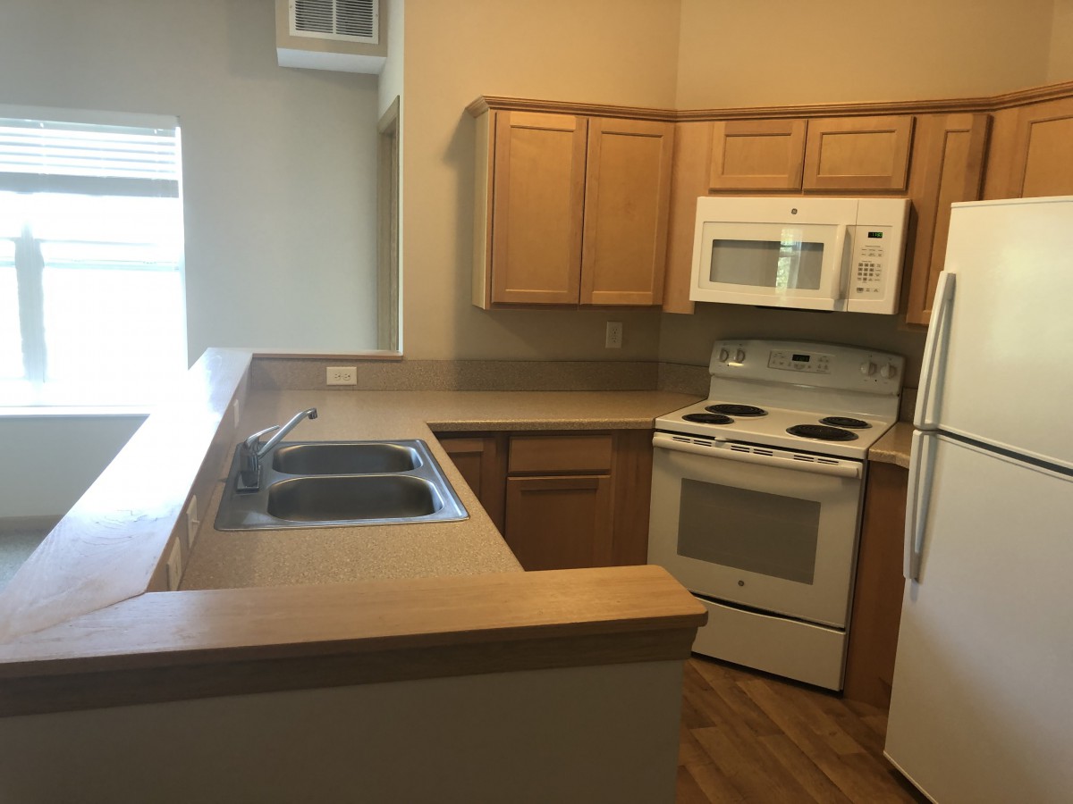 An empty apartment kitchen with wooden cabinets and standard appliances.