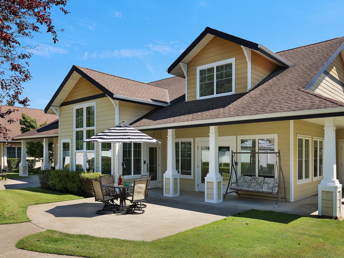 A charming residential house with a spacious backyard patio and outdoor seating, set in a sunny landscape.