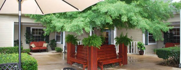An outdoor patio with wooden seating and lush greenery under a large umbrella.