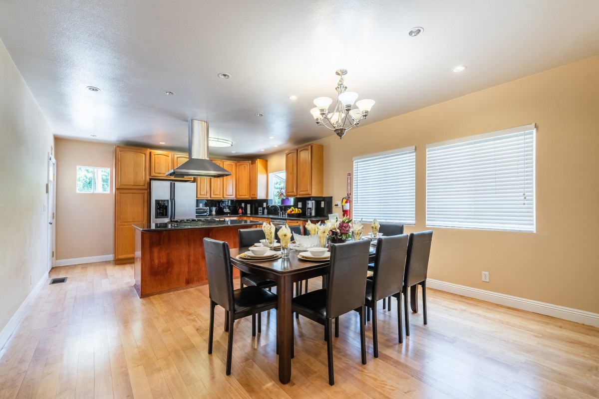 A modern dining area with a spacious kitchen, featuring a large table and chairs, illuminated by a chandelier.