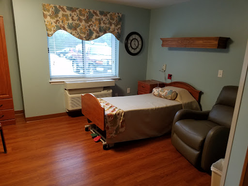 A clean and simple hospital patient room featuring a bed, chair, and window.