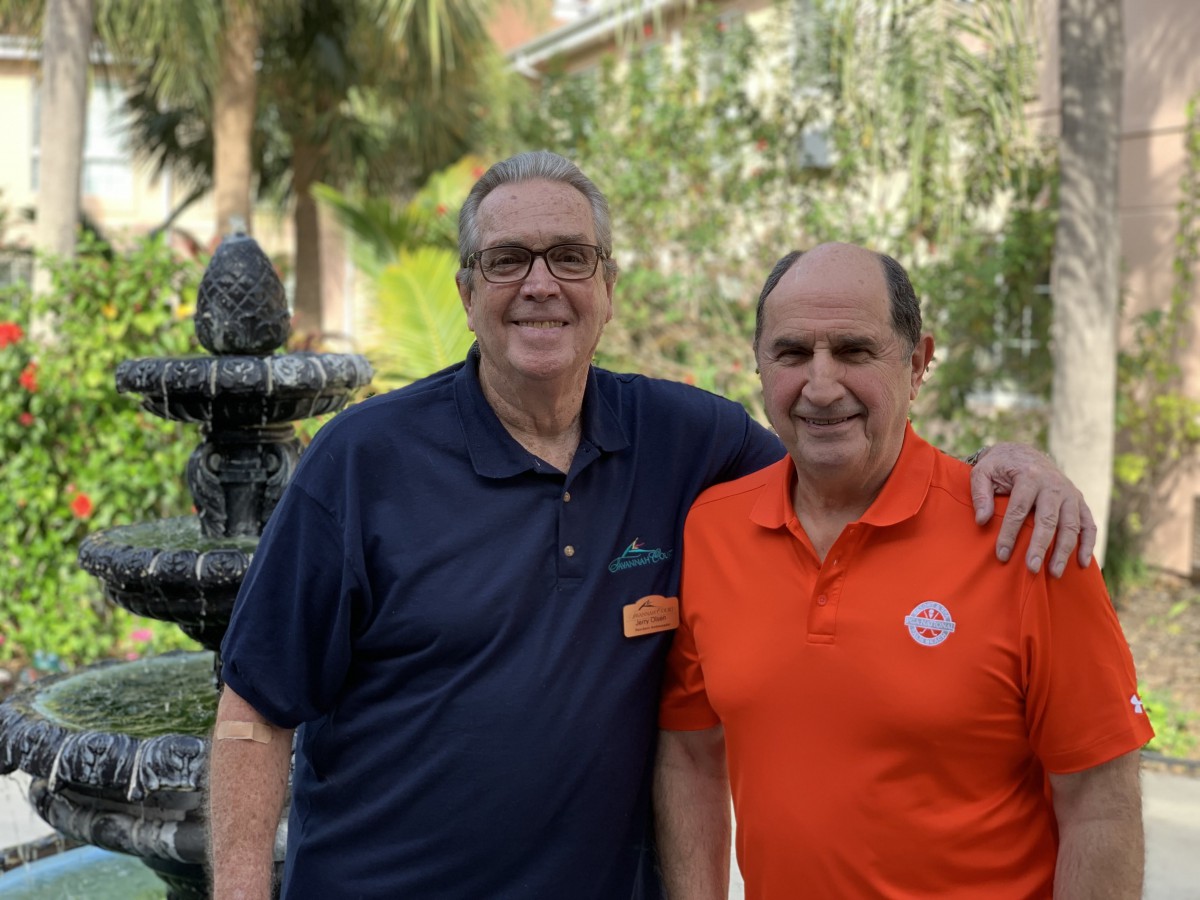 Two smiling men posing together outdoors in casual attire.