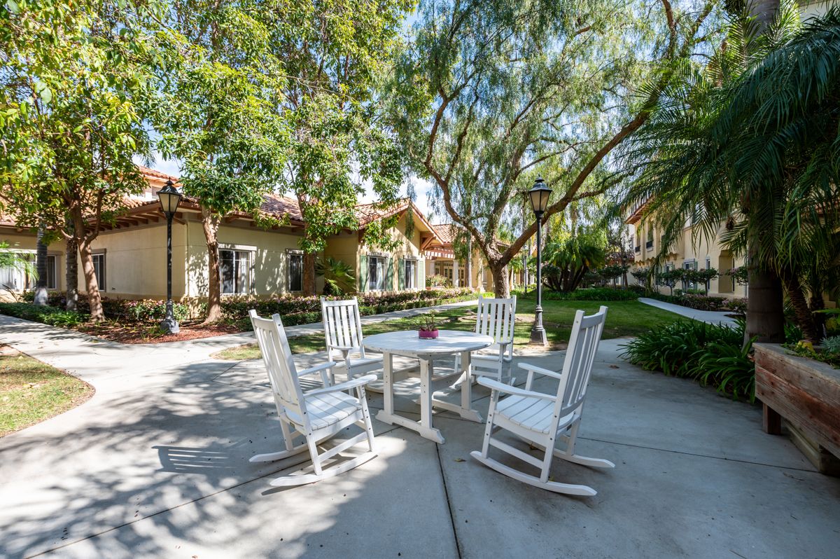 An inviting outdoor patio area with white rocking chairs and a table under shaded trees.