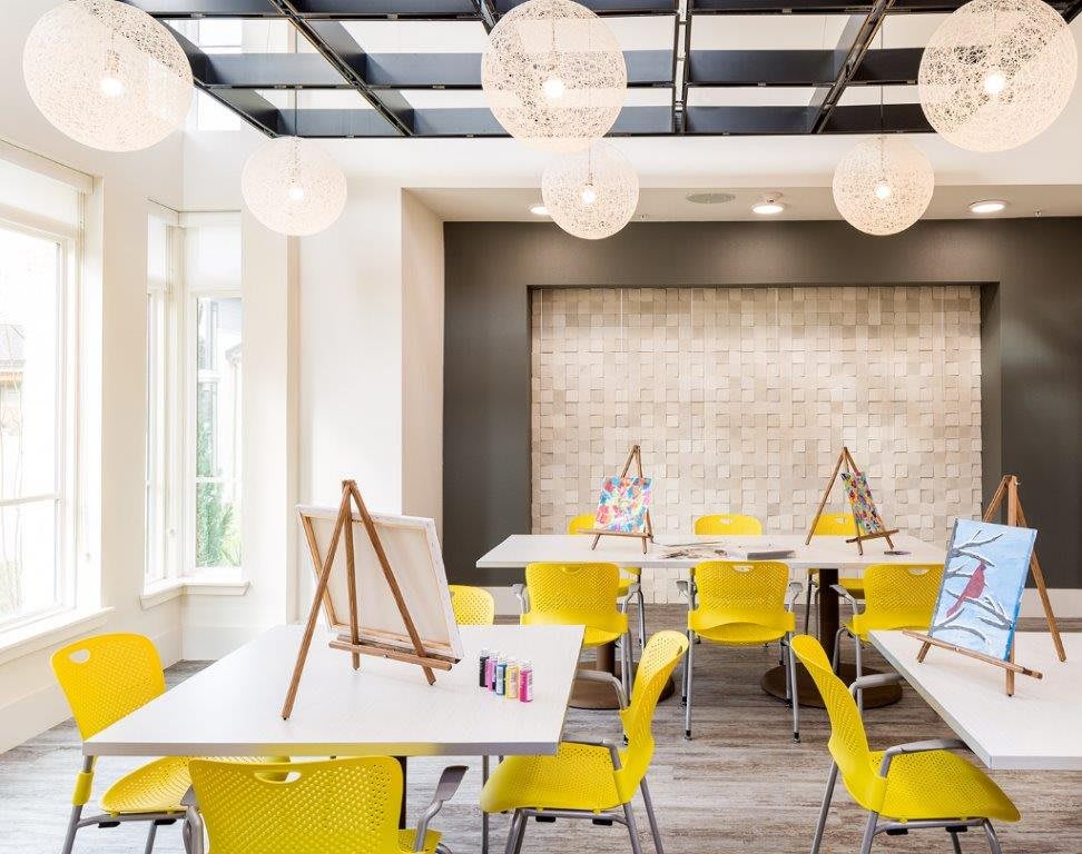 A bright and modern art classroom with yellow chairs and easels, featuring stylish hanging lights.