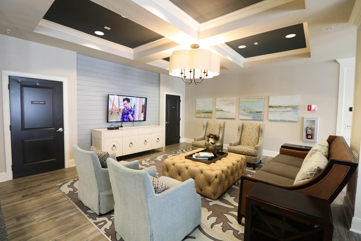 A modern living room with elegant interior design, featuring a chandelier, comfortable seating, and a mounted television.