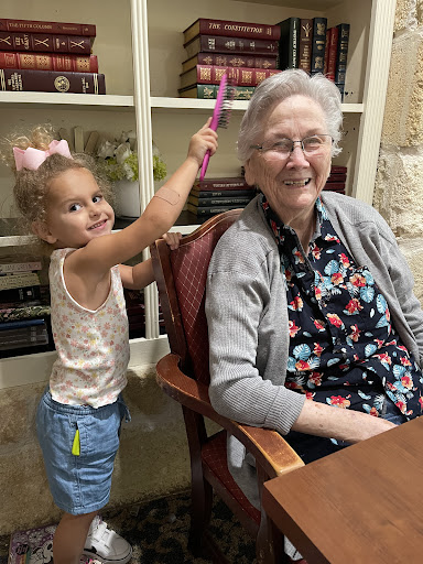 A joyful moment between a young girl and her grandmother, sharing smiles and a playful hair styling session.