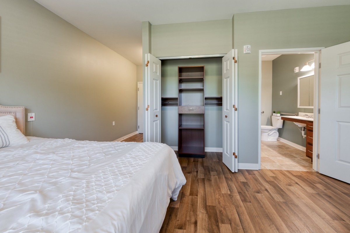 A minimalist bedroom with an open closet and hardwood flooring.
