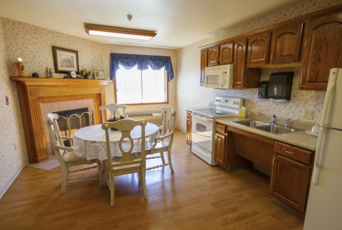 A cozy kitchen with a dining area, featuring wooden cabinets and a fireplace.