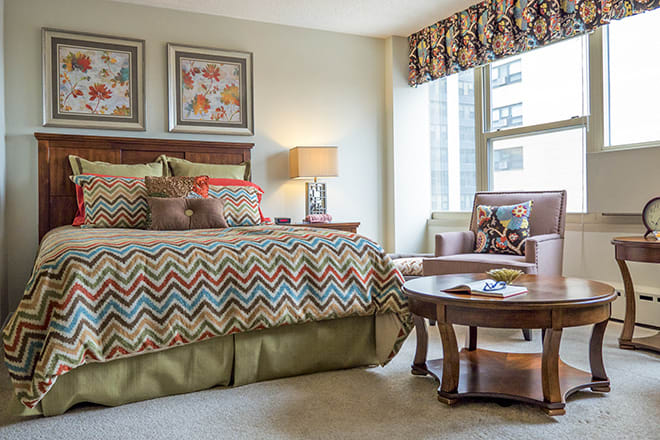 Cozy bedroom with a patterned bedspread, armchair, and window view.