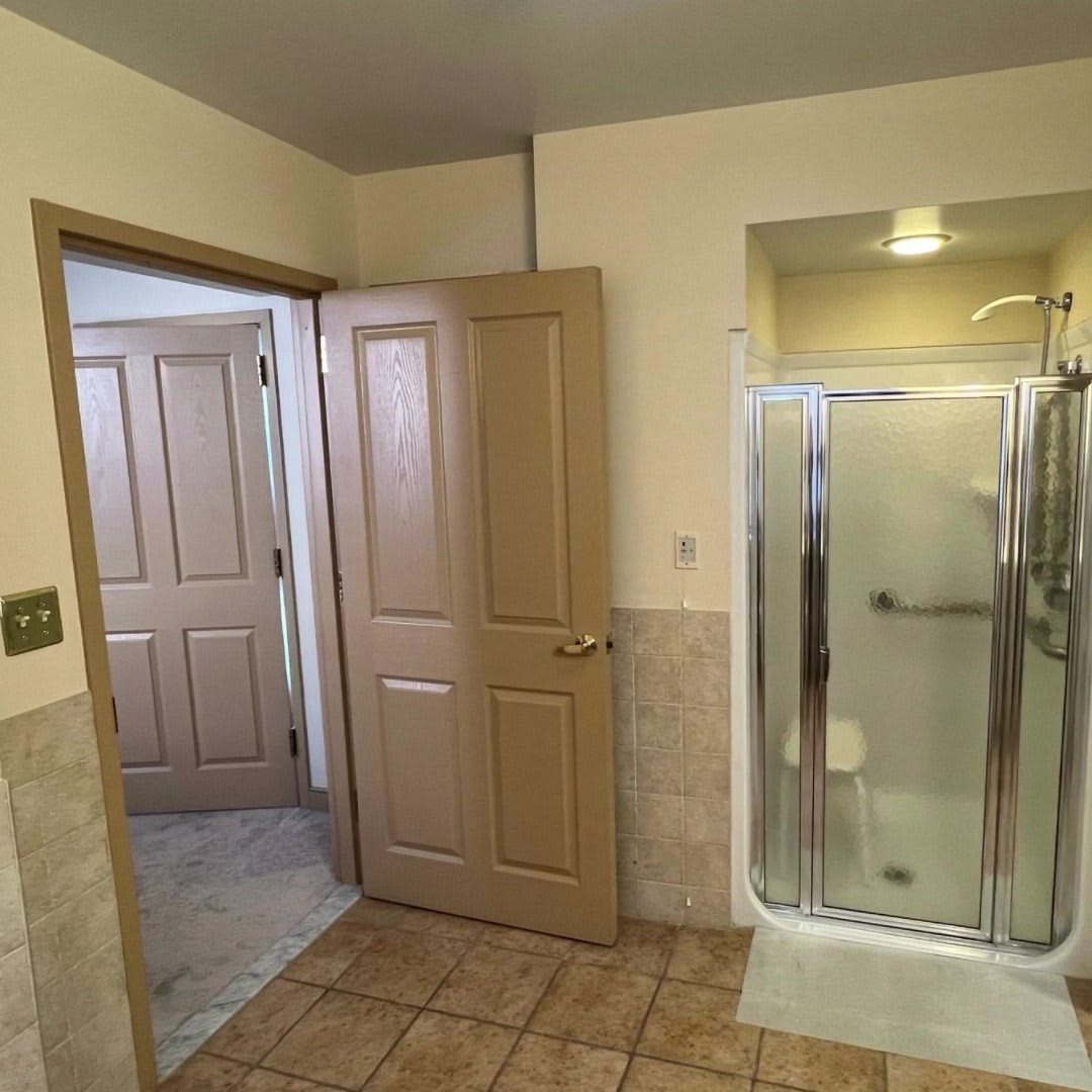 A spacious bathroom featuring a shower, tiled floor, and two wooden doors.