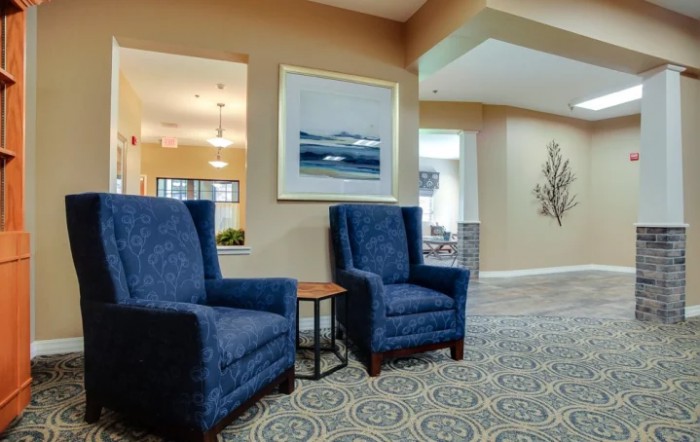 A cozy lobby area featuring two blue armchairs, a small side table, and framed artwork on the wall.