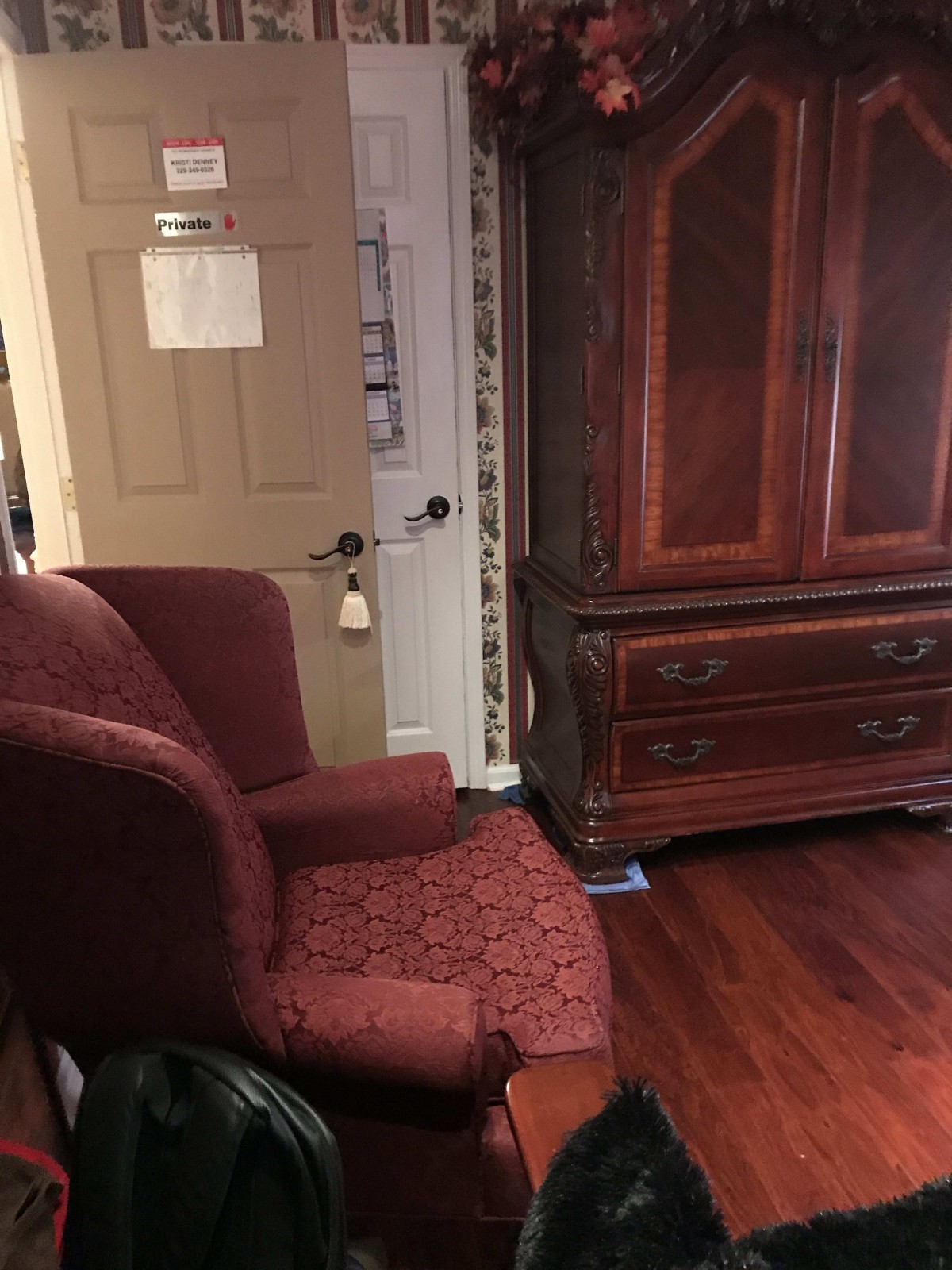 A cozy room featuring a red armchair and a large wooden cabinet next to the door.