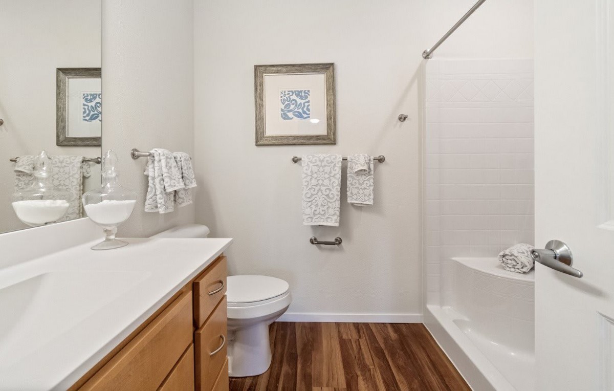A modern bathroom with wooden flooring, featuring a toilet, sink, and shower area.