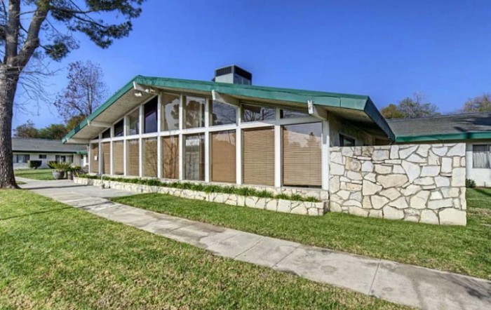 A mid-century modern house with large glass windows and a green roof.