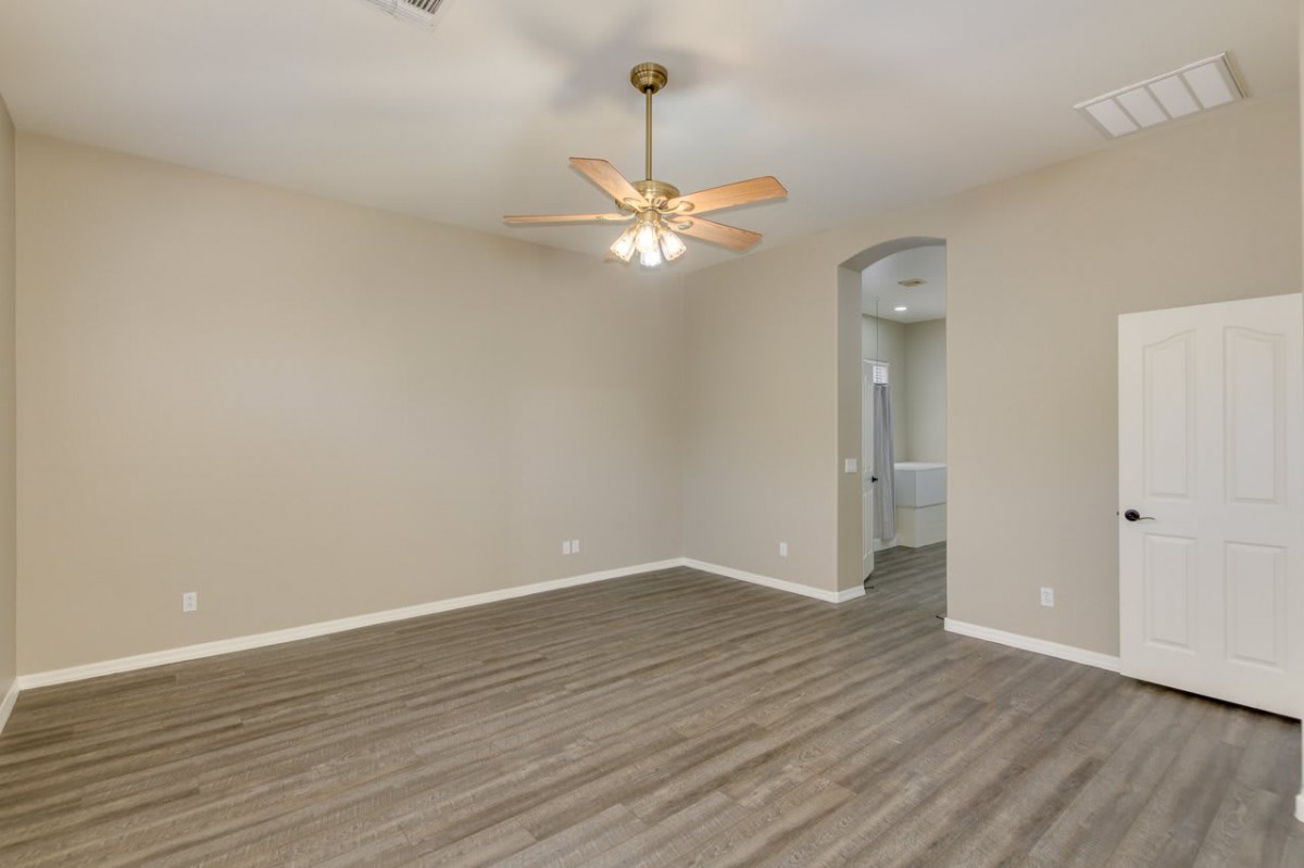 An empty room with neutral walls, a hardwood floor, and a ceiling fan.