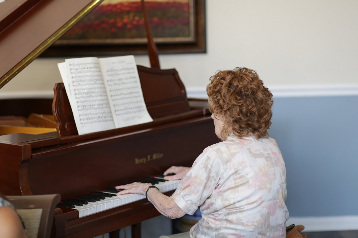 An older woman playing the piano while reading sheet music.