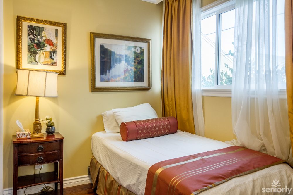 A cozy bedroom with a single bed, adorned with warm-toned curtains and artwork on the walls.