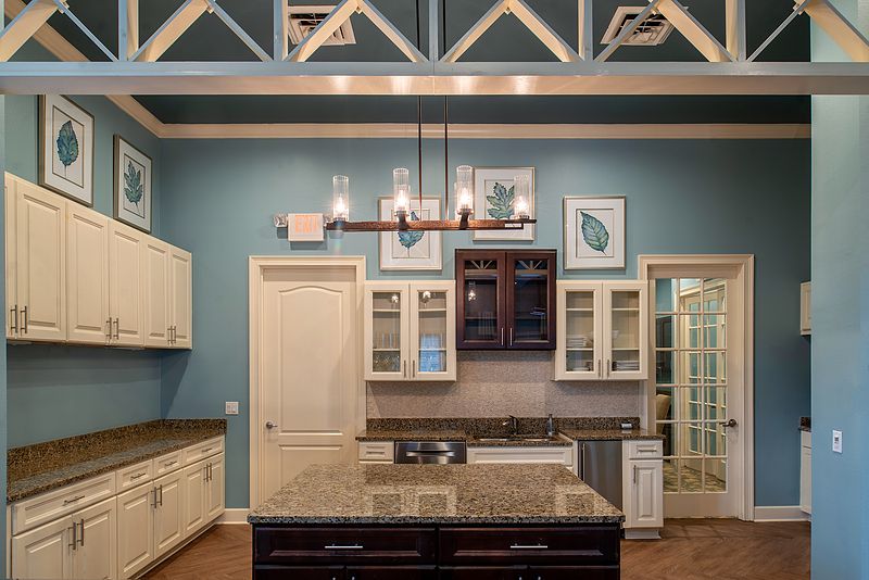 A beautifully designed kitchen with blue walls, featuring an island with a granite countertop and a stylish chandelier.