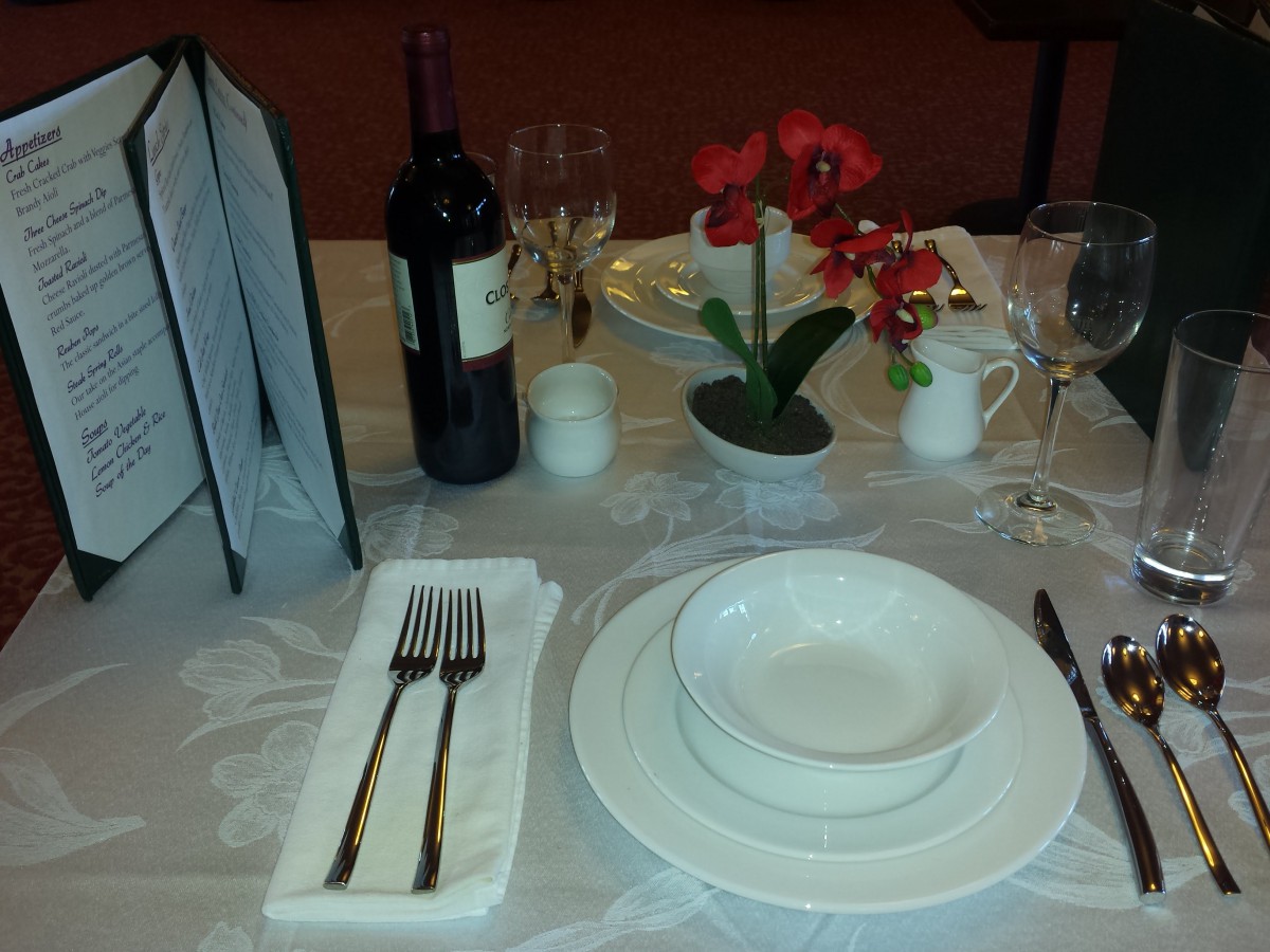 Elegant dining table setup with wine, plates, cutlery, and a flower centerpiece.