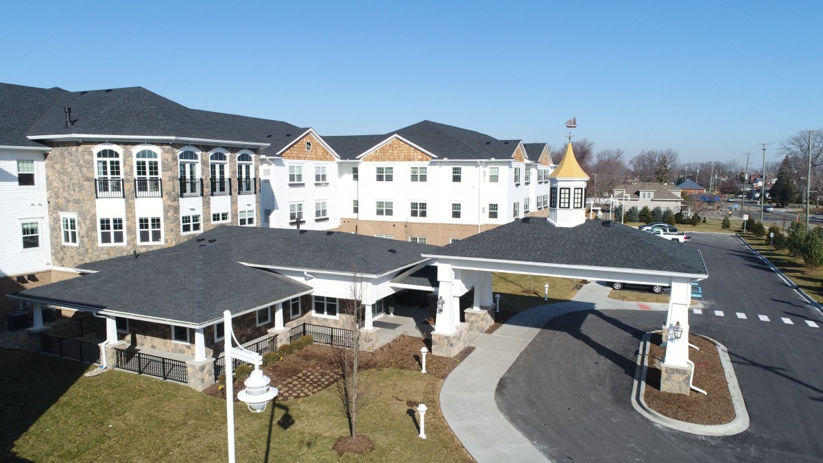 A large, multi-story assisted living building with a driveway and landscaped surroundings.