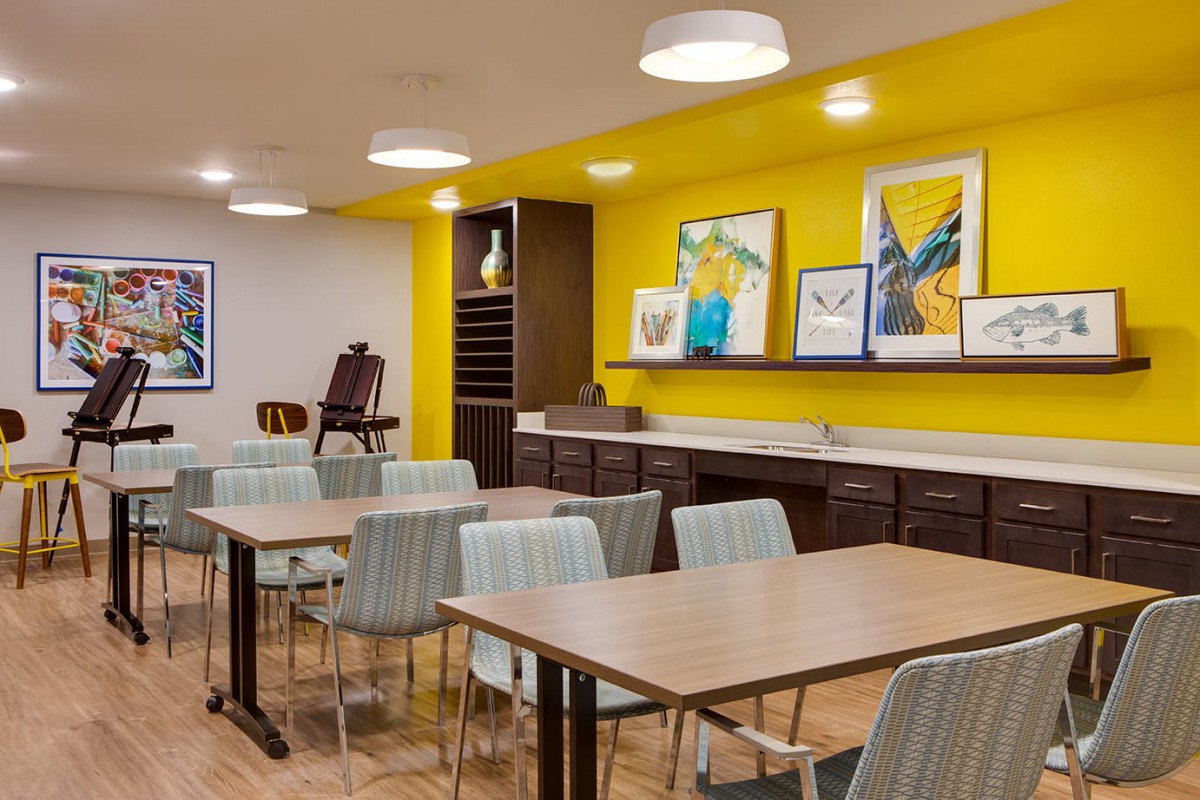 A modern dining area with stylish furniture and colorful artwork on a yellow accent wall.
