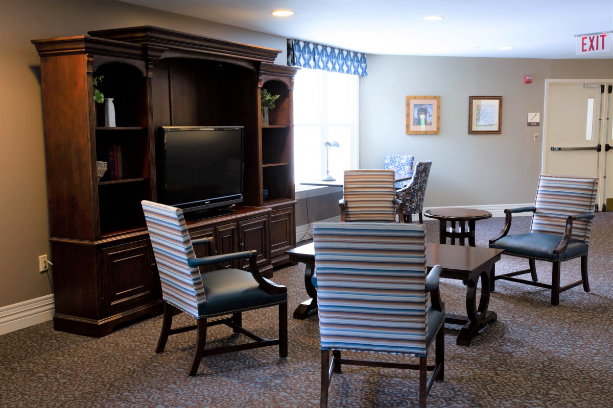 A cozy living area with striped chairs, wooden tables, a large television, and bookshelves against the wall.
