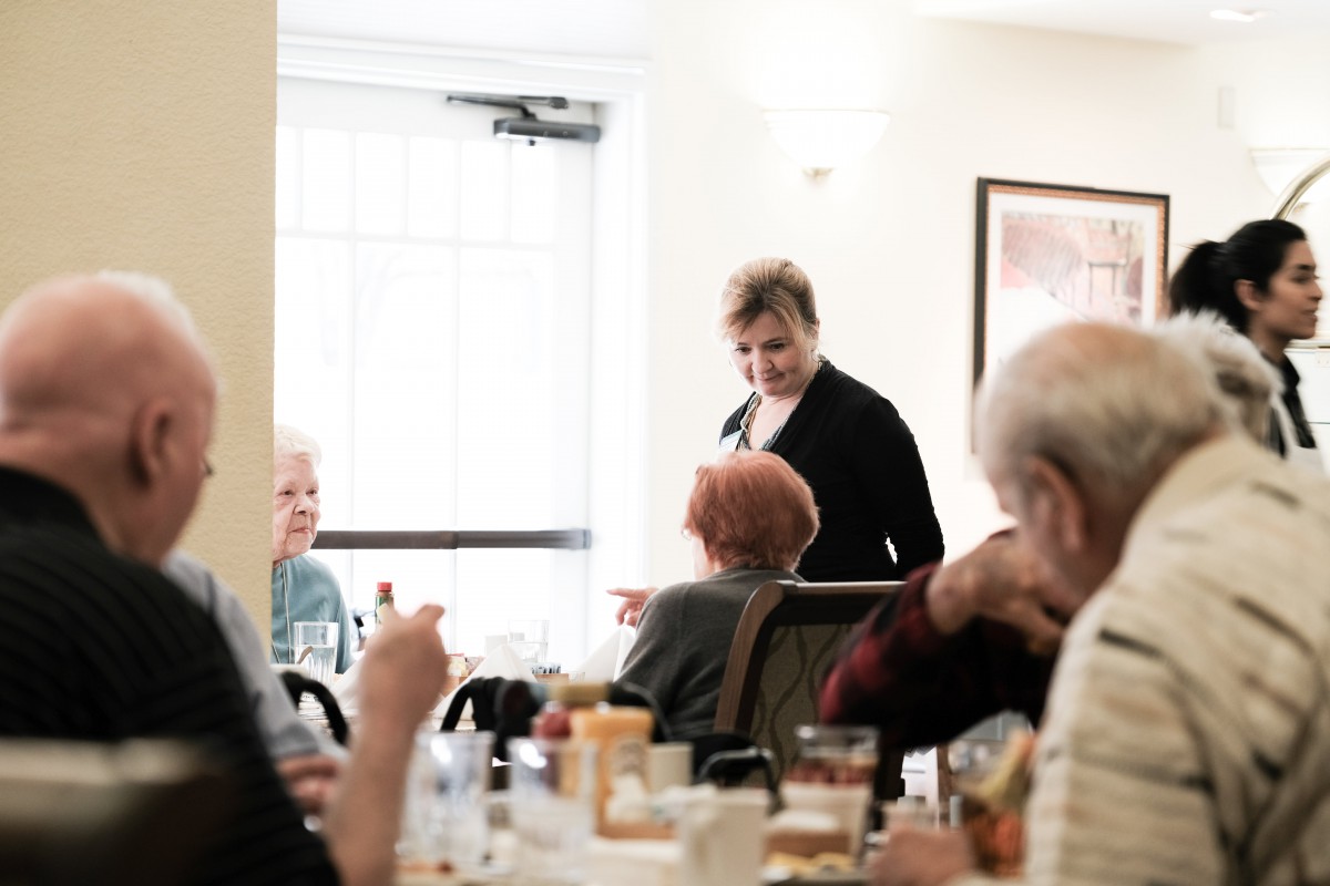 Elderly individuals enjoying a meal and conversation in a dining setting.