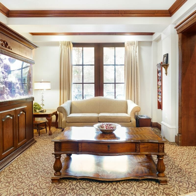 A traditional living room with wooden furniture, a sofa, and large windows.