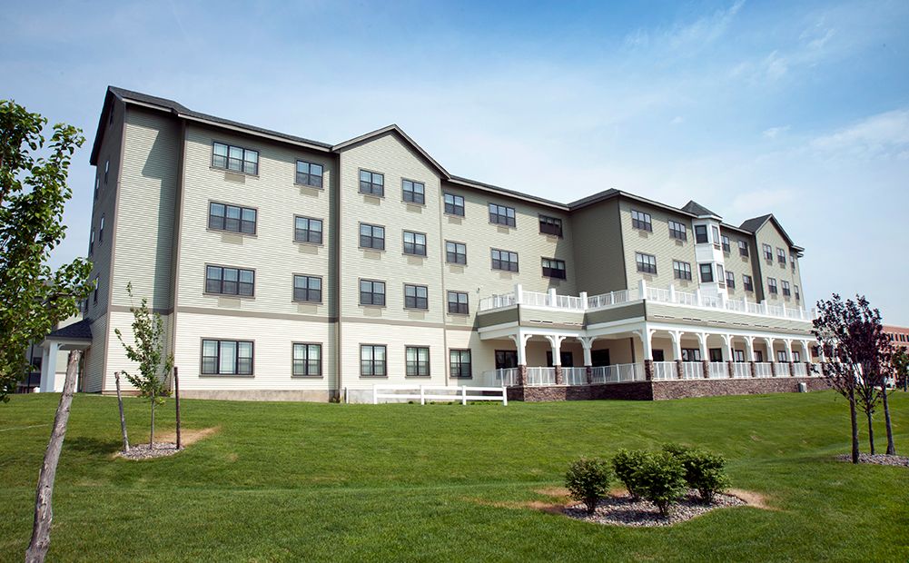 A multi-story residential building with a well-maintained lawn and outdoor porch area.