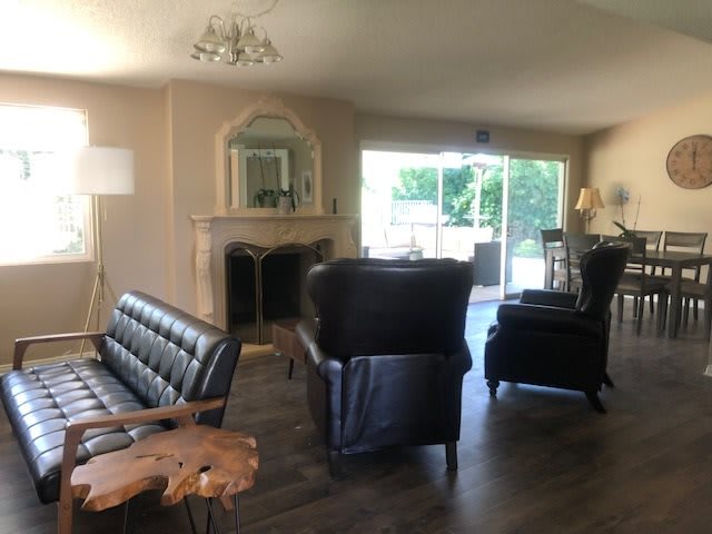 A cozy living room featuring leather seating, a fireplace adorned with a mirror, and a sliding glass door that lets in natural light.