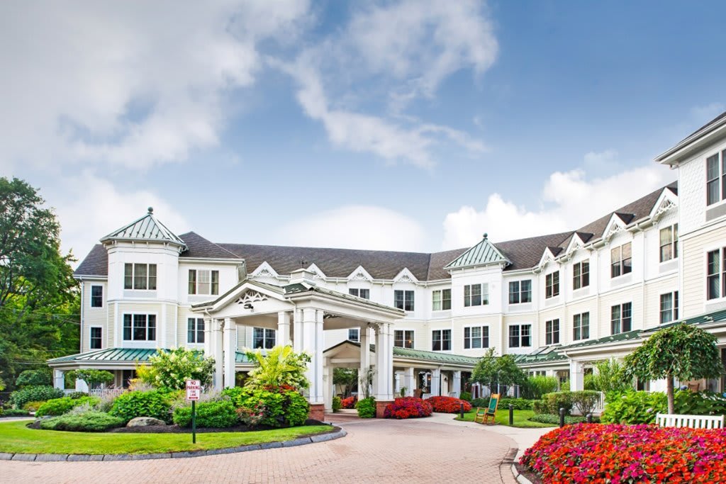 A grand, white building surrounded by lush gardens under a blue sky.