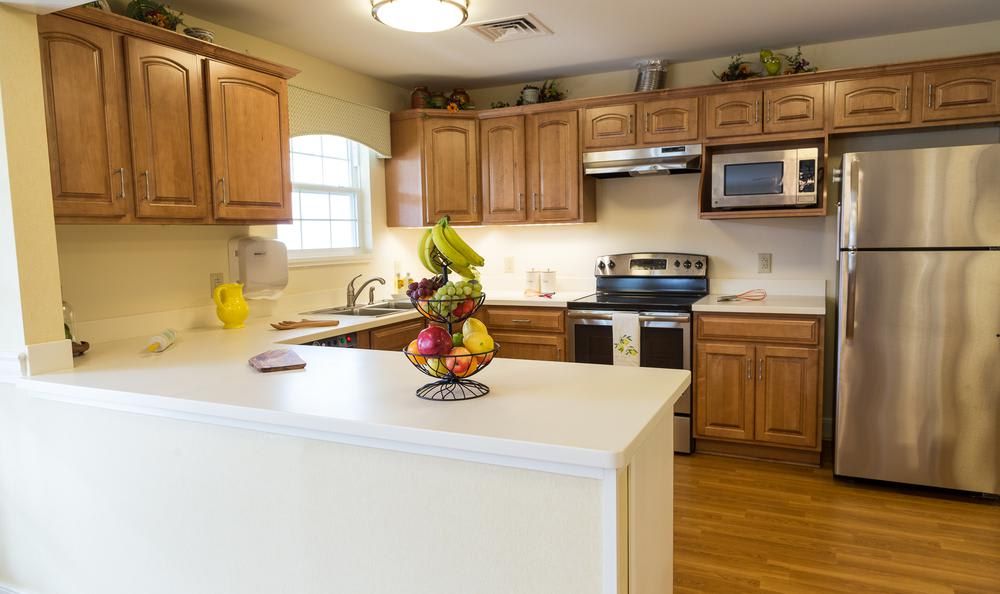 A cozy kitchen with wooden cabinets, a white countertop featuring a fruit basket, and modern appliances.
