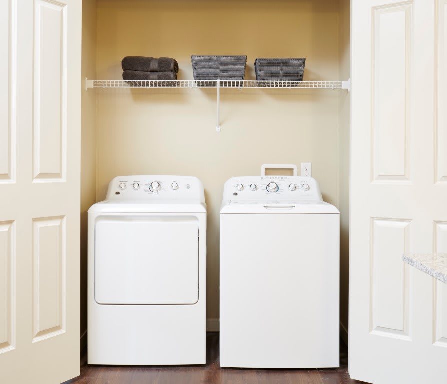 A small laundry room with a washer and dryer beneath a storage shelf.