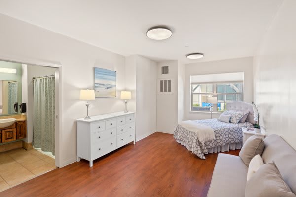 A bright and cozy bedroom with a bed, dresser, and ample lighting.