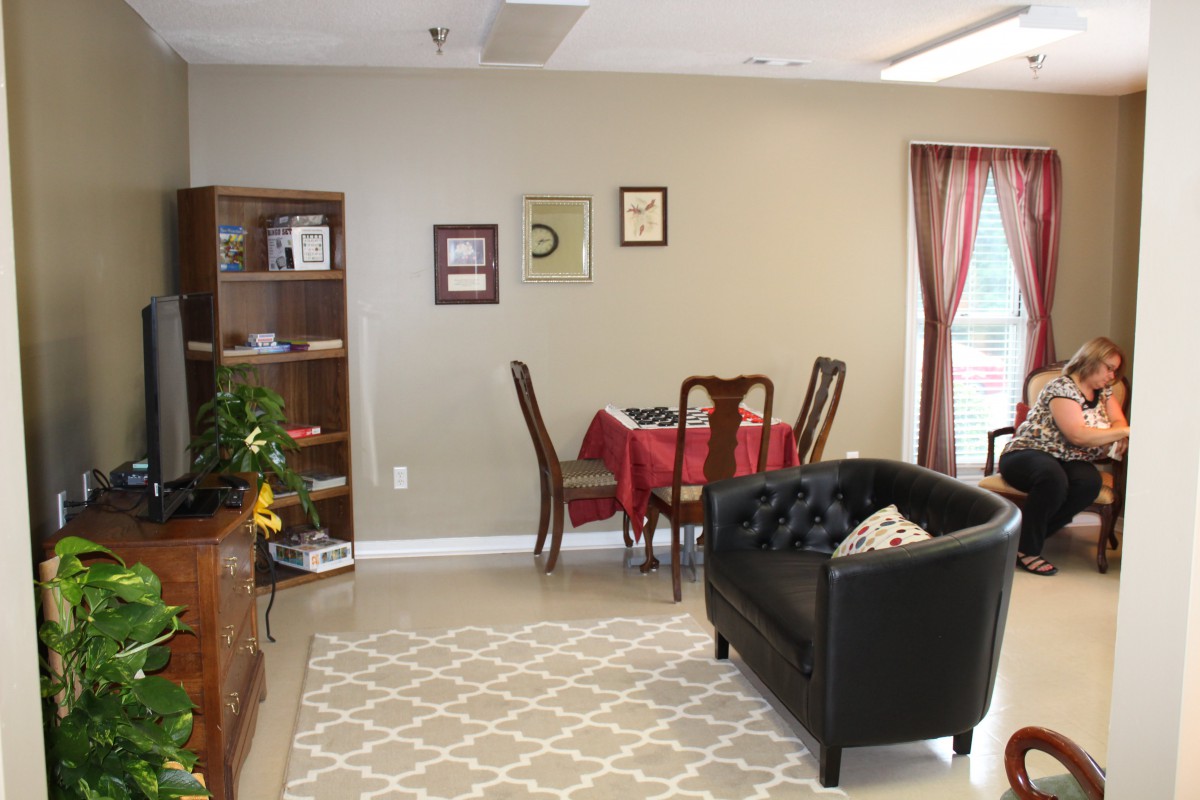 A cozy living room with a small dining area, featuring a bookshelf, couch, and carpet.