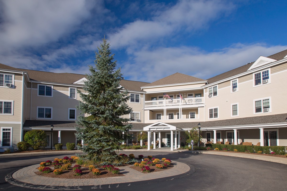 A large residential building with a central entrance, landscaped surroundings, and a partially cloudy sky.