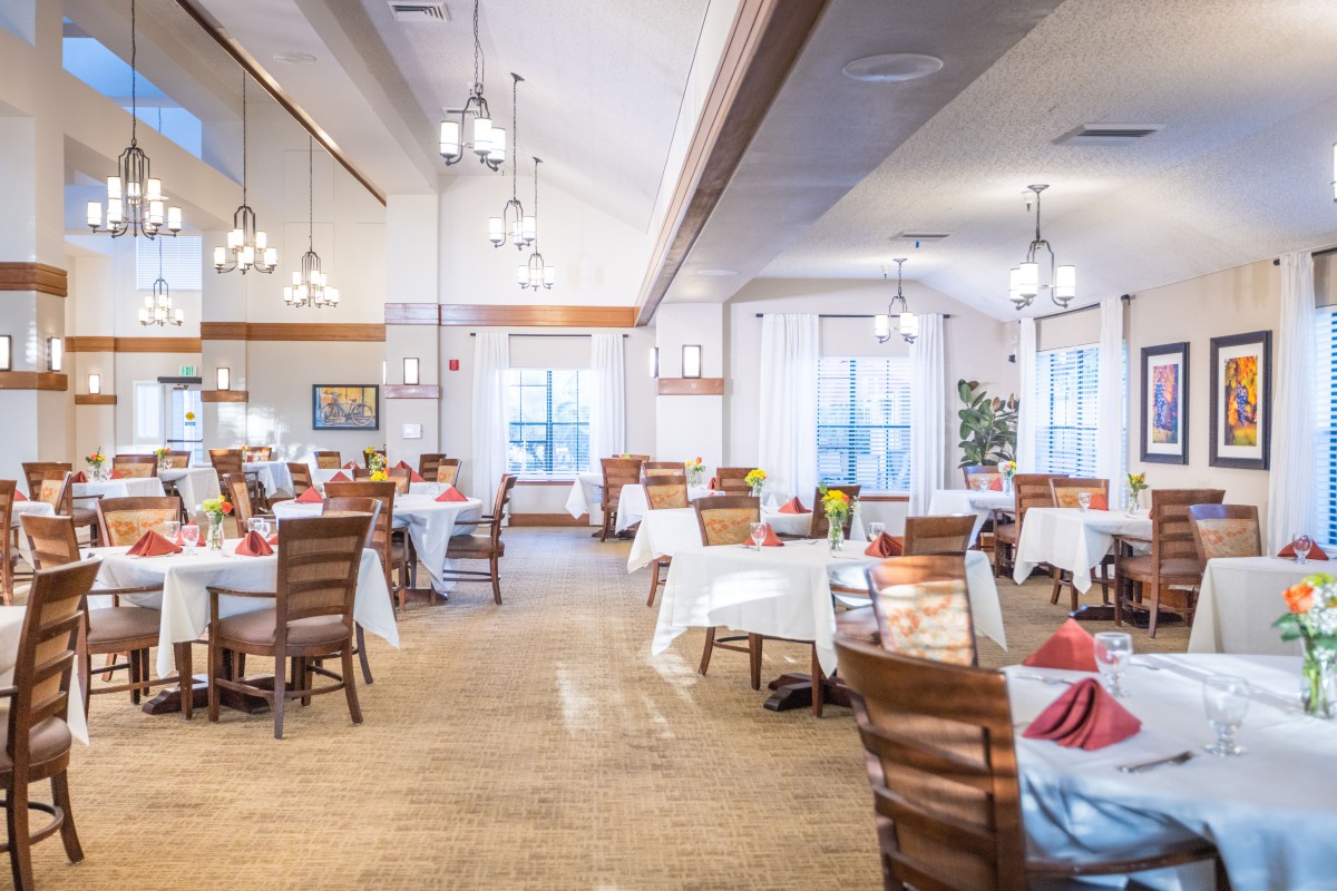 A spacious dining area featuring neatly arranged tables with white tablecloths, wooden chairs, and elegant chandeliers.