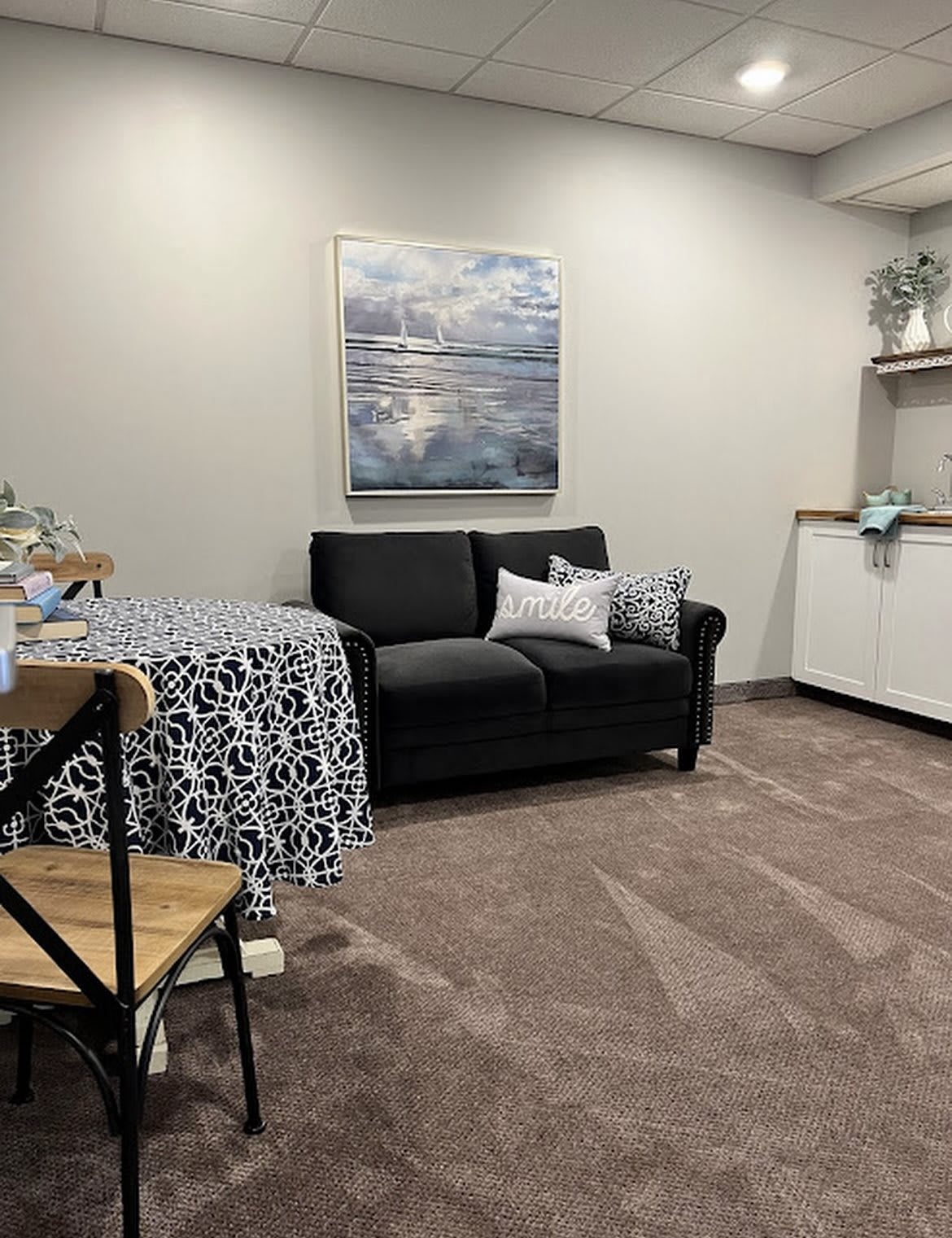 A cozy living room setup with a black sofa, decorative pillows, and a patterned tablecloth.