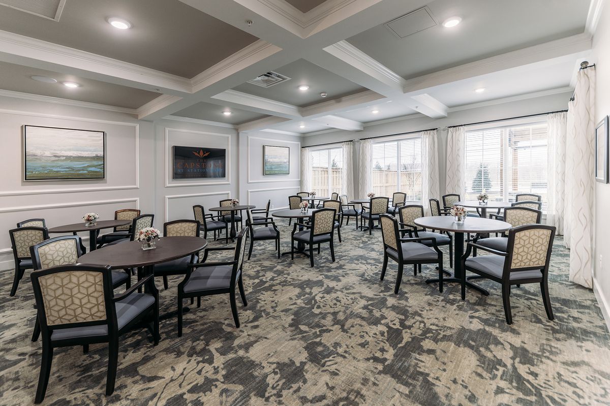 A modern dining room with multiple tables and chairs, featuring elegant lighting and a wall-mounted television.