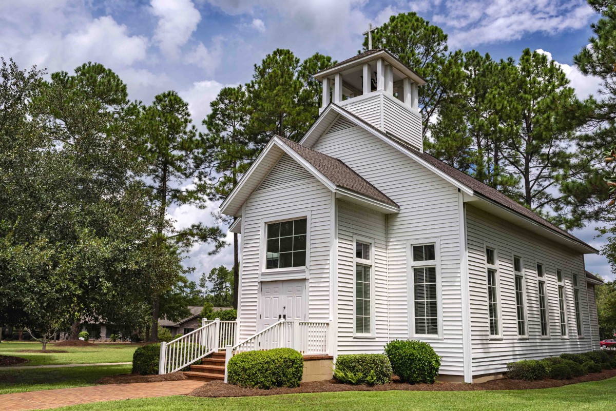 A quaint white church surrounded by trees under a clear sky.