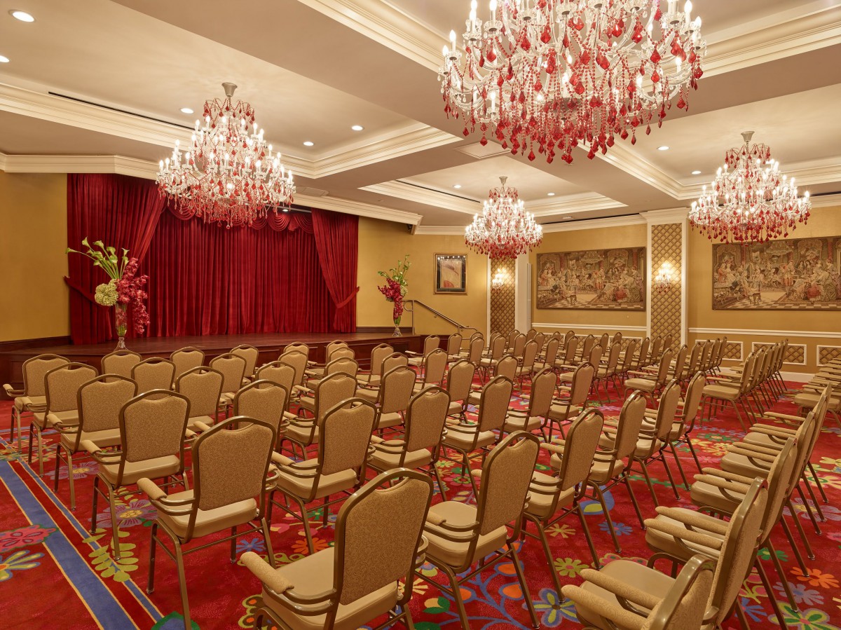 An elegant conference room with chandeliers and arranged seating facing a stage.