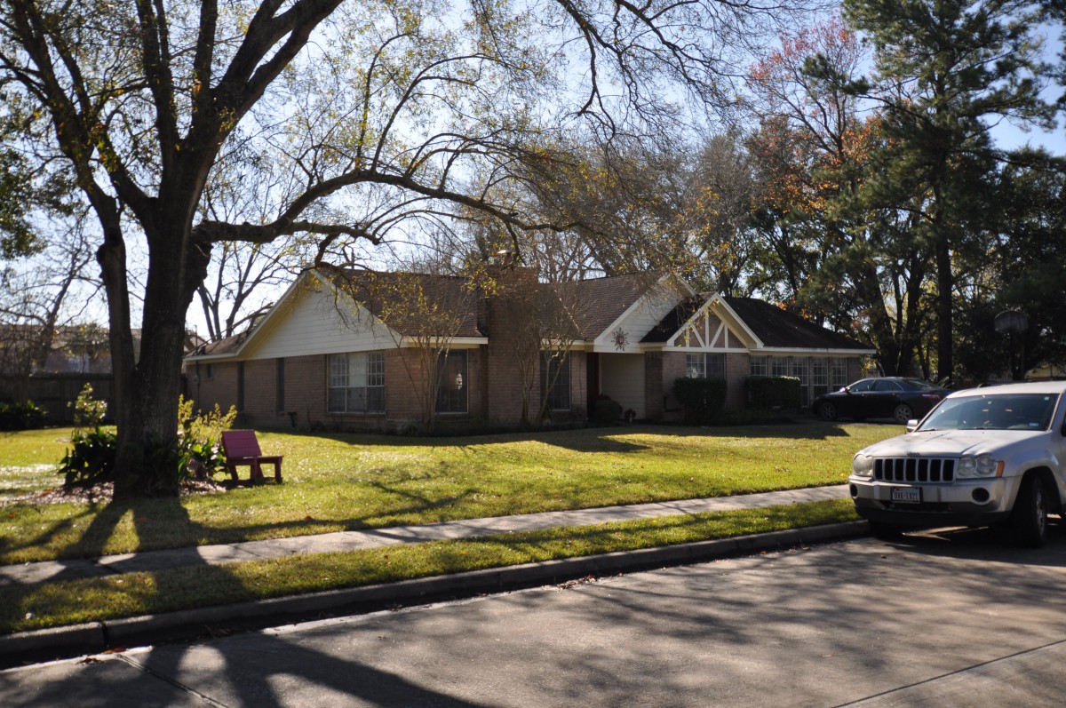 A suburban house with a well-kept lawn and trees on a sunny day.
