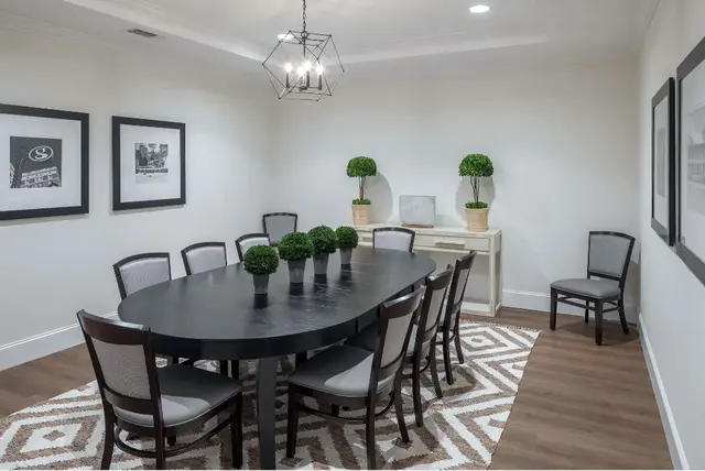 A modern dining room with a black oval table, surrounded by chairs and decorated with green plants and wall art.