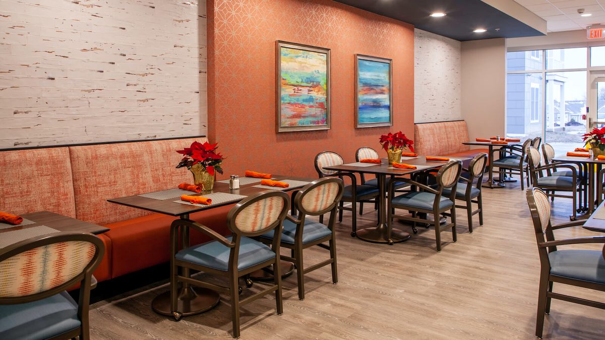 A cozy restaurant interior featuring neatly arranged tables and chairs, decorated with vibrant paintings and potted plants.