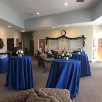 A reception area with blue tablecloths and floral arrangements on high tables.
