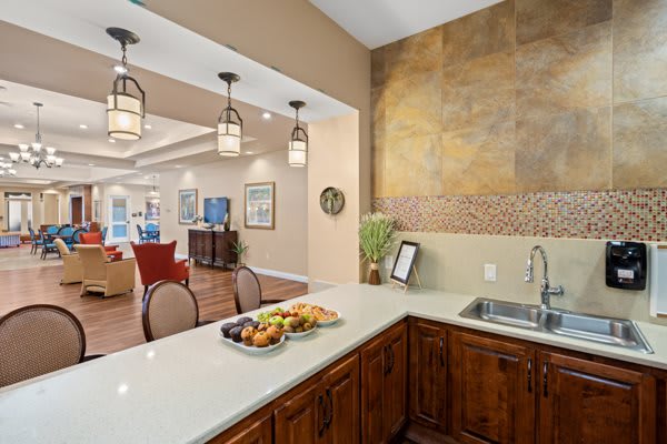 A modern kitchen with a light-colored countertop, featuring a fruit plate and sink, connected to an open-concept living area.