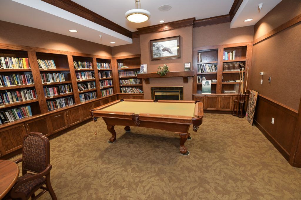 A cozy library interior featuring bookshelves, a fireplace, and a billiards table.