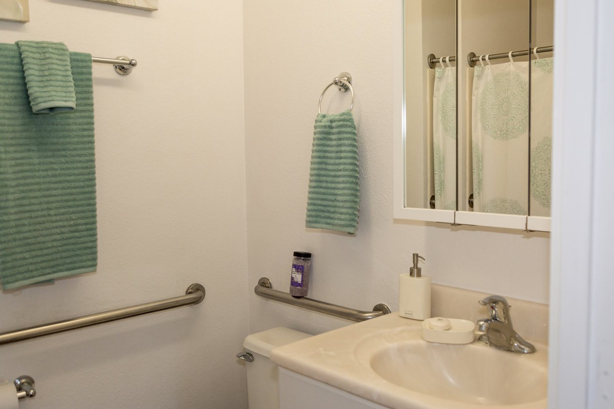A bathroom with a sink, mirror, and handrails.